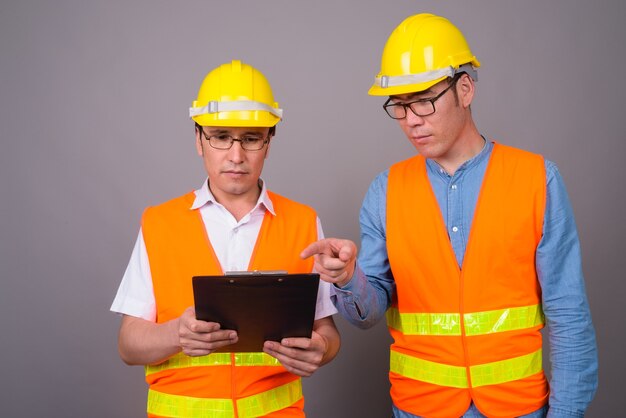 Deux jeunes hommes asiatiques ouvrier du bâtiment ensemble contre mur gris