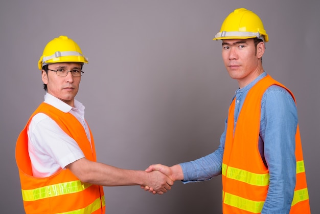 Deux Jeunes Hommes Asiatiques Ouvrier Du Bâtiment Ensemble Contre Mur Gris