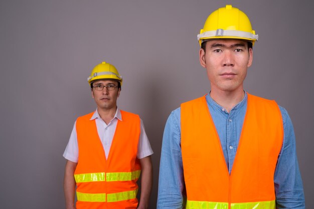 Deux jeunes hommes asiatiques ouvrier du bâtiment ensemble contre mur gris