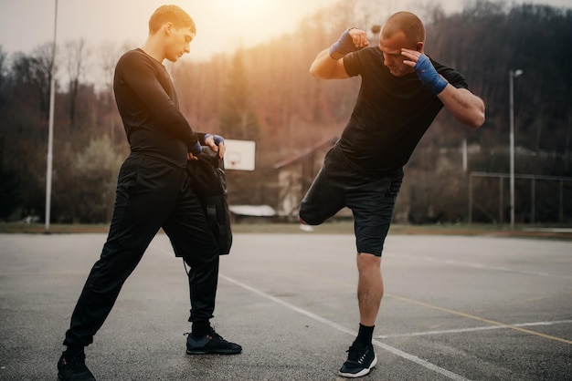 Deux jeunes hommes athlétiques boxe Hommes s'entraînant à l'extérieur Entraînement kickboxingDeux mâles boxant à l'extérieur