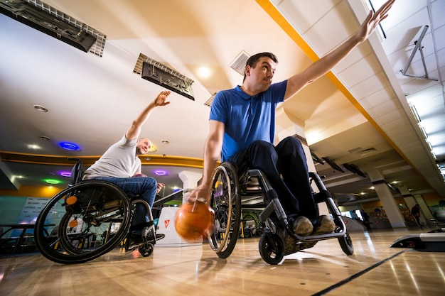 Deux jeunes hommes handicapés en fauteuil roulant jouant au bowling dans le club