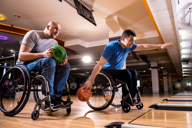 Deux jeunes hommes handicapés en fauteuil roulant jouant au bowling dans le club