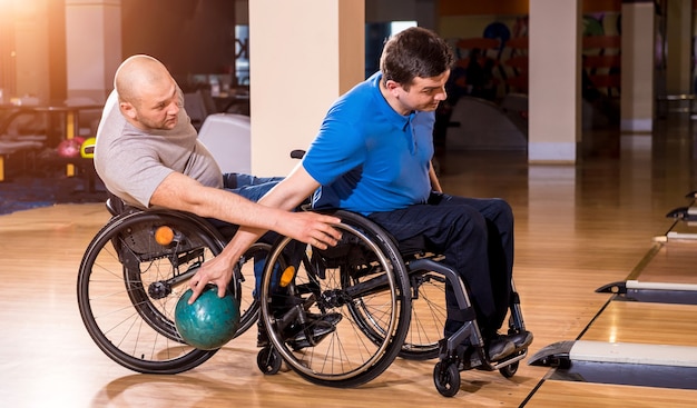 Deux jeunes hommes handicapés en fauteuil roulant jouant au bowling dans le club