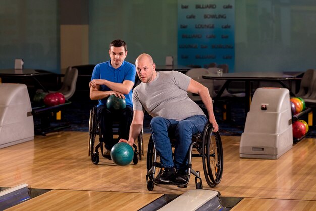 Deux jeunes hommes handicapés en fauteuil roulant jouant au bowling dans le club