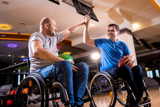 Deux jeunes hommes handicapés en fauteuil roulant jouant au bowling dans le club