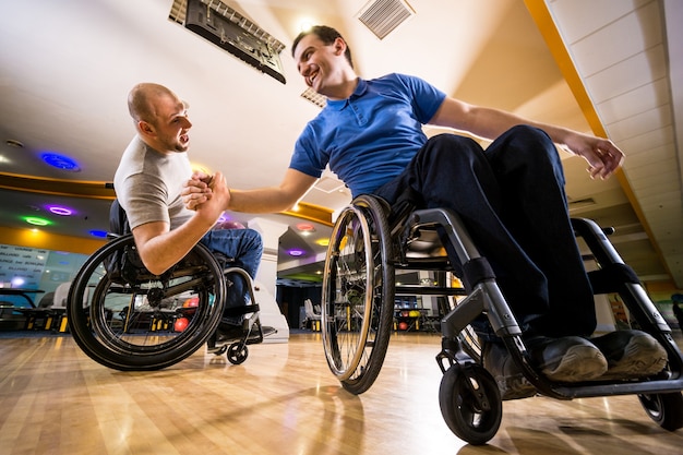 Deux jeunes hommes handicapés en fauteuil roulant jouant au bowling dans le club