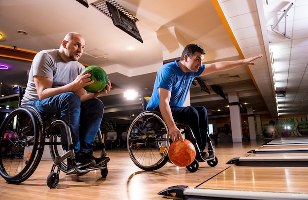 Deux jeunes hommes handicapés en fauteuil roulant jouant au bowling dans le club