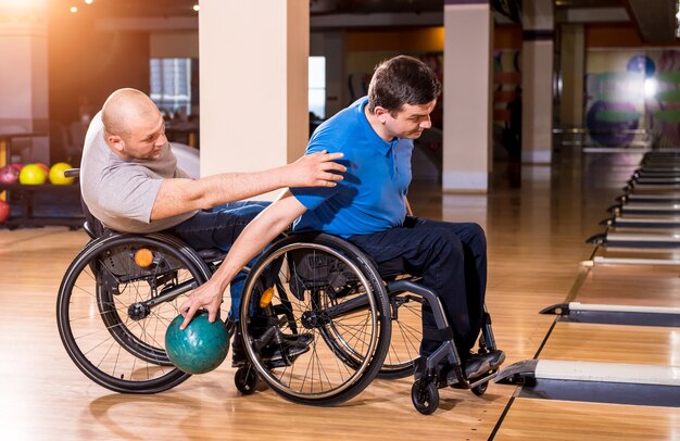 Deux jeunes hommes handicapés en fauteuil roulant jouant au bowling dans le club