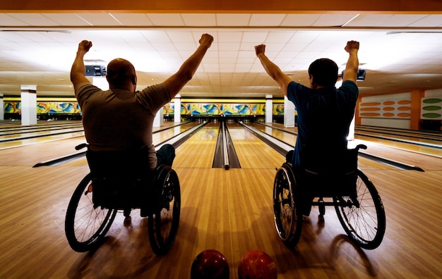 Deux jeunes hommes handicapés en fauteuil roulant jouant au bowling dans le club