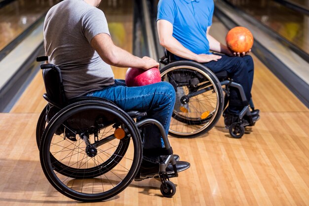 Deux jeunes hommes handicapés en fauteuil roulant à jouer au bowling dans le club