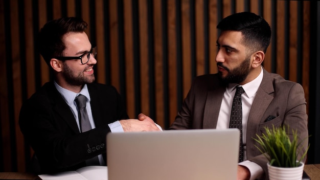 Deux jeunes hommes sourient et se serrent la main lorsqu'ils se rencontrent à la table du bureau de l'entreprise