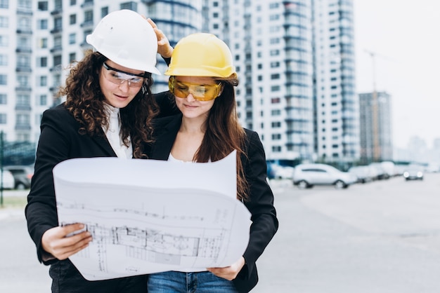 Deux jeunes ingénieurs industriels de jeunes femmes d&#39;affaires dans des casques de construction sur un fond en verre. Plan de construction, architecte, designer, succès