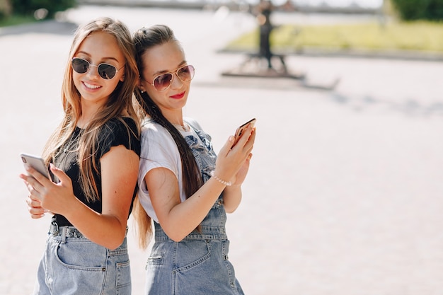 Photo deux jeunes jolies filles en promenade dans le parc avec des téléphones. journée d'été ensoleillée, joie et amitiés.