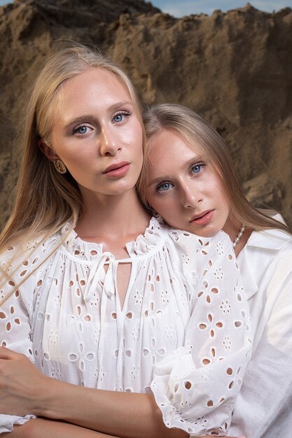 Deux jeunes jolies jumelles aux longs cheveux blonds posant à la carrière de sable dans d'élégantes robes blanches