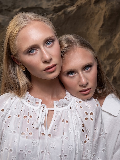 Deux jeunes jolies jumelles blondes posant à la carrière de sable dans d'élégants vêtements blancs