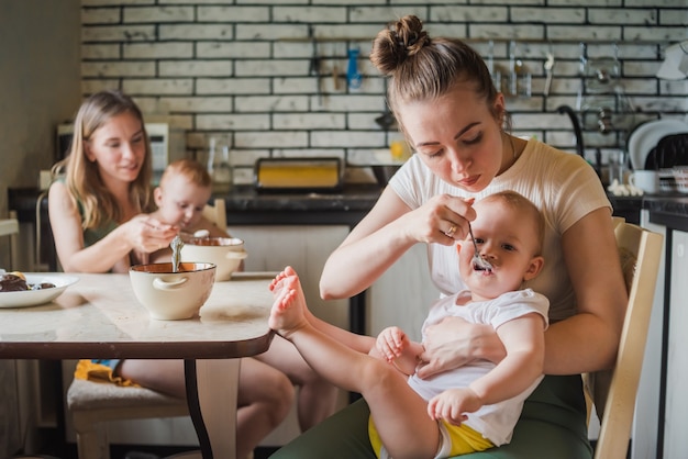 Deux Jeunes Mères Ensemble Nourrissent Leurs Bébés Heureux Bouillie De Lait Dans La Cuisine