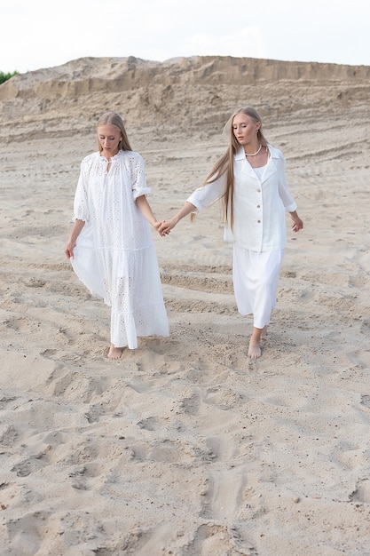 Deux jeunes soeurs jumelles attrayantes posant à la carrière de sable dans des vêtements blancs élégants