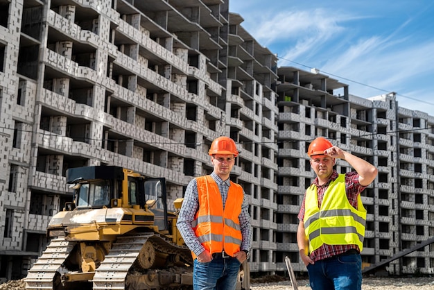 Deux jeunes travailleurs forts en uniforme se tiennent sur le fond d'un nouveau bâtiment Le concept d'un nouveau bâtiment