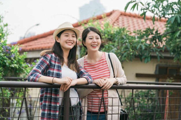 deux jolies amies japonaises asiatiques en vêtements de printemps debout en plein air s'appuyant sur la balustrade et regardant vers le bas tout en visitant le monument dans le petit village. beauté amitié féminine entourée d'arbres