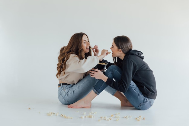 Deux jolies amies de jeunes filles gaies debout isolées sur fond blanc, mangeant du pop-corn