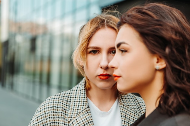 Deux jolies amies posant près d'un bâtiment en verre. Couple de filles lesbiennes gays étreignant embrassant