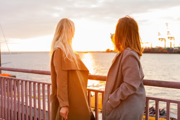 Deux jolies copines femmes en manteaux d'automne au lever du soleil à la mer