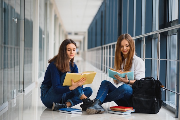 Deux jolies étudiantes avec des livres assis sur le sol dans le couloir de l'université