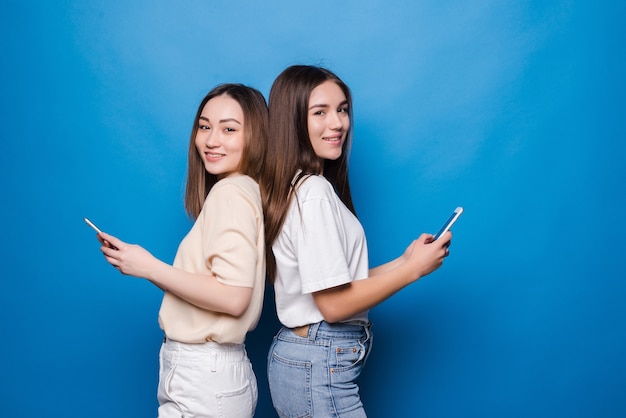 Deux jolies femmes à l'aide de téléphones portables sur un mur bleu