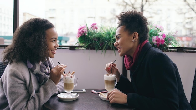 Deux jolies femmes métisses parlant et buvant du café dans un café de rue