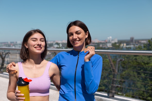 Deux jolies femmes en tenue de sport sur les amis du pont, parler heureux et positif en marchant sourire, profitant du matin de remise en forme, vue imprenable sur la ville