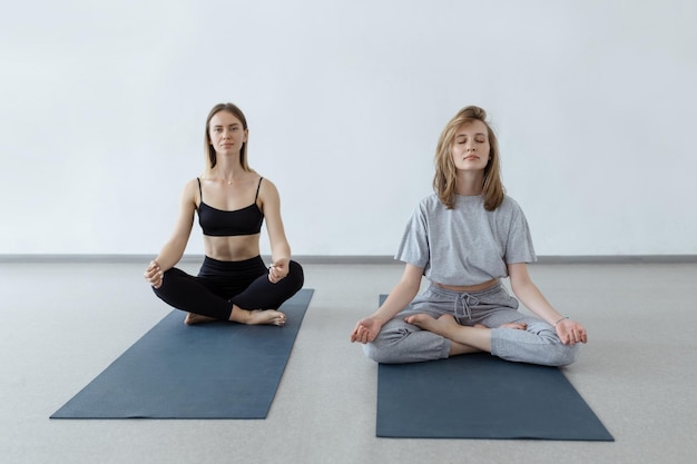 Deux jolies filles athlétiques s'assoient en position du lotus sur un tapis de yoga à l'intérieur Yoga fitness et mode de vie sain