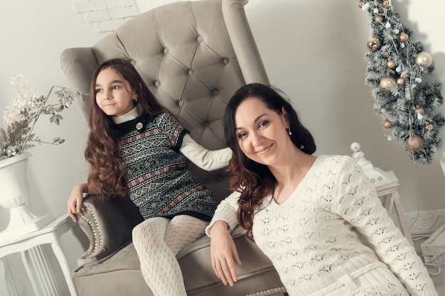 Deux jolies filles, une mère et sa fille installées sur un sol dans une chambre décorée pour Noël.