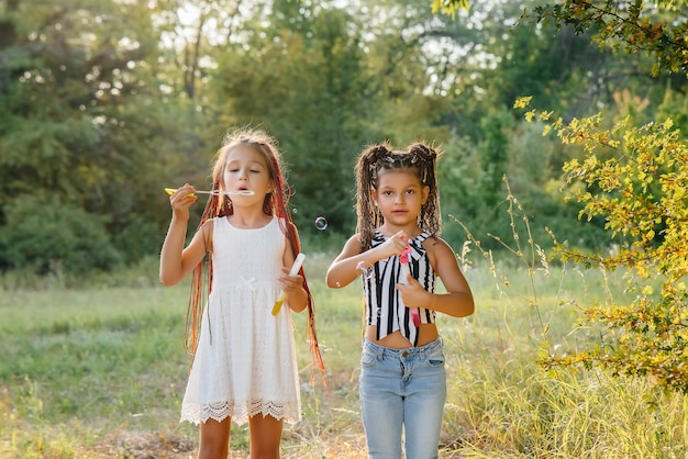 Deux jolies filles avec des nattes jouent dans le parc en faisant exploser des bulles de savon.