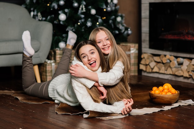 Deux jolies filles posant avec l'expression du visage qui s'embrasse à la fête d'anniversaire. Dame européenne aux cheveux longs debout à côté de l'arbre et des cadeaux