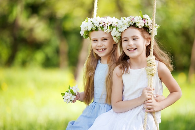 Deux jolies filles s'amusant sur une balançoire dans le vieux jardin de pommiers en fleurs. Journée ensoleillée. Activités de plein air printanières pour les enfants