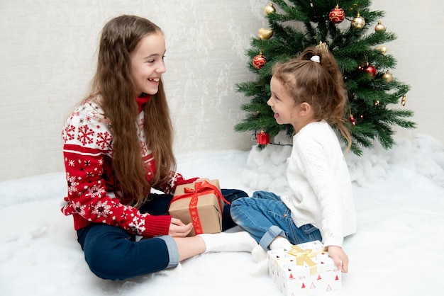 Deux jolies filles souriantes s'assoient à côté de l'arbre de Noël et se donnent des cadeaux Nouvel An Noël