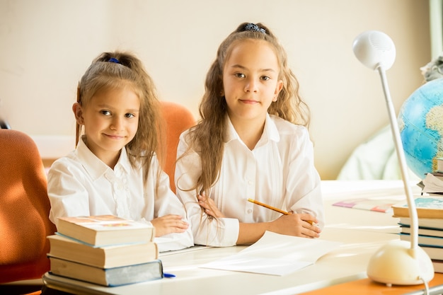 Deux jolies filles en uniforme scolaire assis au bureau et à faire leurs devoirs