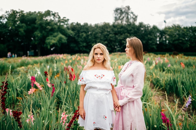 Deux jolies jeunes amies en robes ethniques se détendre dans le jardin fleuri en été.