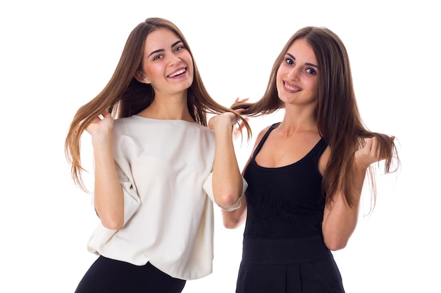 Deux jolies jeunes femmes en chemises noires et blanches touchant les cheveux sur fond blanc en studio