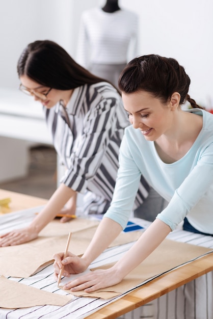 Deux jolies jeunes femmes traçant des motifs sur des tissus, utilisant des crayons pour cela et semblant totalement impliquées dans le processus