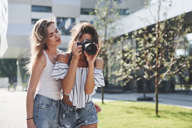 Deux jolies jolies amies de la fille avec l'appareil photo prennent des photos ensemble et se promènent en ville