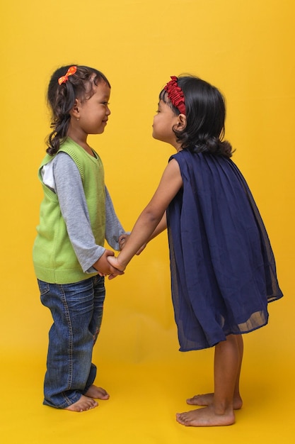 deux jolies petites filles asiatiques se tenant par la main et se regardant sur un fond jaune