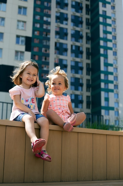 Deux jolies petites filles assises à l'extérieur dans un paysage urbain. Génération alpha. Format vertical, sœurs