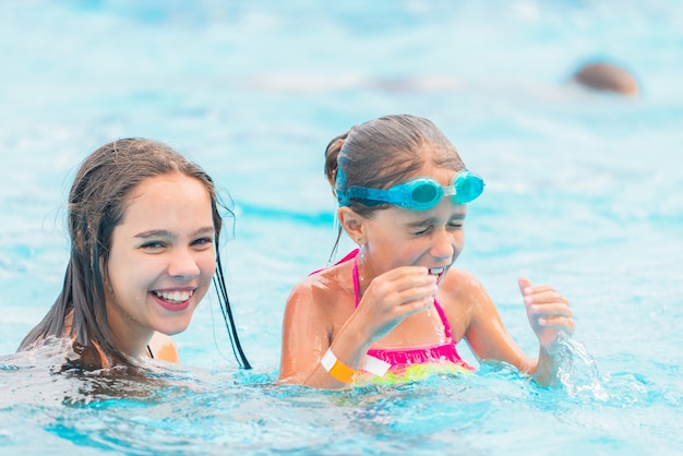 Deux jolies petites filles sœurs nagent dans la piscine pendant les vacances par une chaude journée d'été ensoleillée