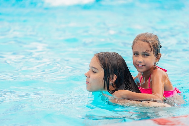 Deux jolies petites filles sœurs nagent dans la piscine pendant les vacances par une chaude journée d'été ensoleillée