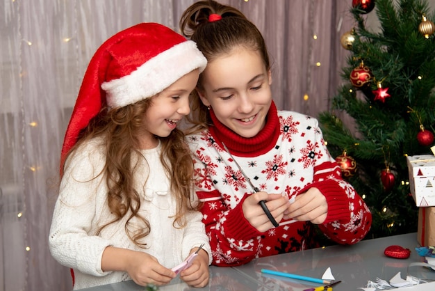 Deux jolies sœurs coupent des flocons de neige dans du papier pour préparer les vacances Nouvel An Noël Confort