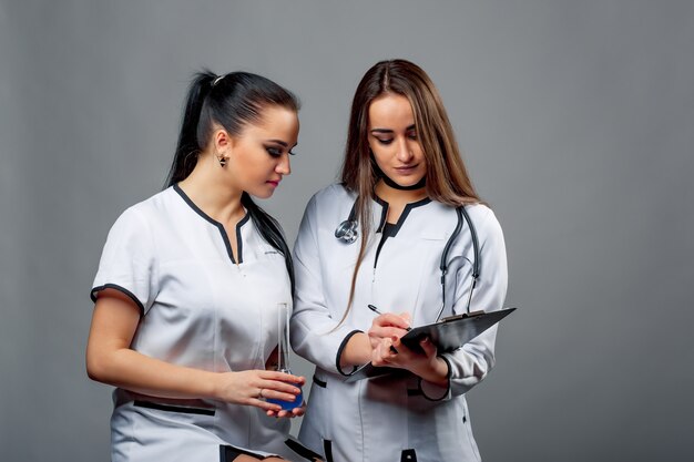Deux jolis médecins portant l'uniforme médical en train de regarder le dossier et discutant du diagnostic sur fond gris