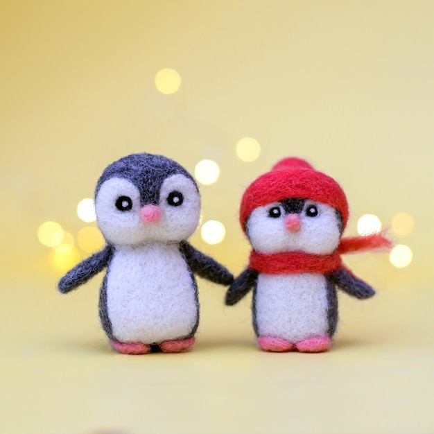 Deux jouets de Noël en laine feutrée mignons petits pingouins sur fond jaune avec bokeh