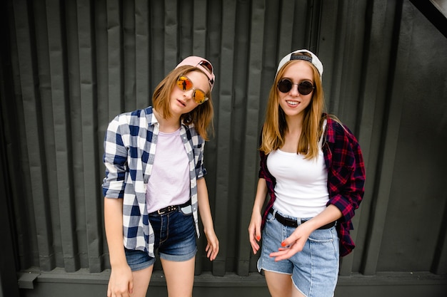 Deux joyeuses filles drôles portant des chemises à carreaux posant contre le mur de la rue dans la rue.