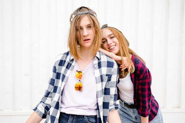 Deux joyeuses filles drôles portant des chemises à carreaux posant contre le mur de la rue dans la rue.